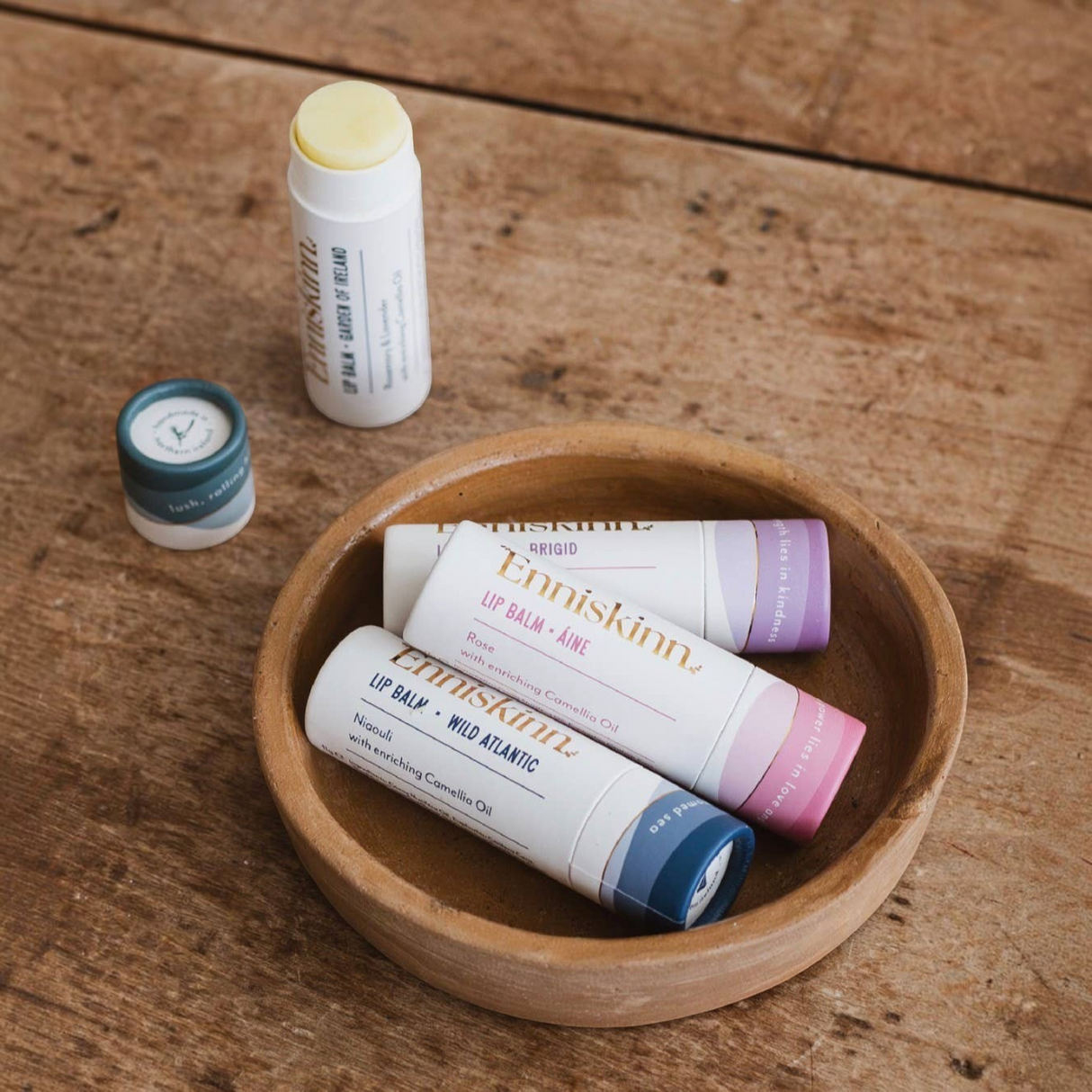 Connemara Country Enniskinn natural lip balms in a wooden bowl on a rustic table, featuring various botanical scents.