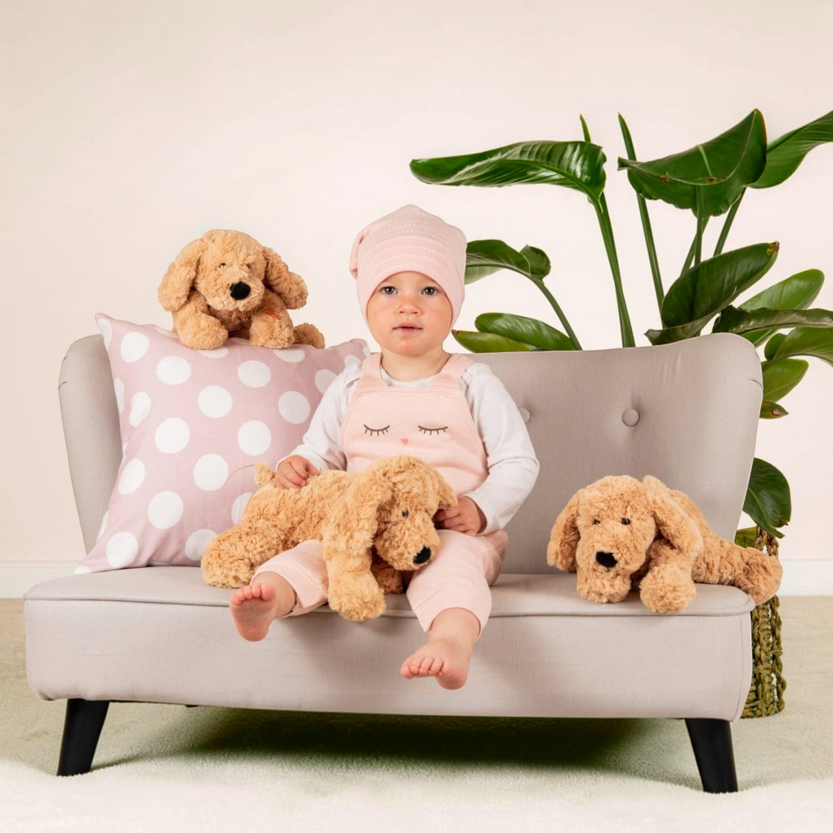 Connemara Country toddler sitting on a small sofa with three beige Teddy Hermann soft plush dogs