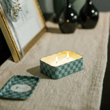 Connemara Country Paddywax A Dopo Lush Palms candle in a green and blue checkered tin burning on a linen runner.