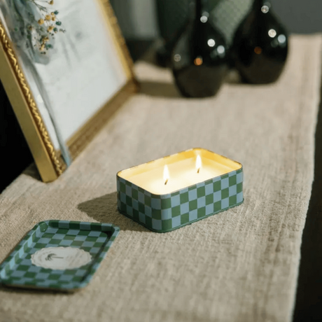 Connemara Country Paddywax A Dopo Lush Palms candle in a green and blue checkered tin burning on a linen runner.