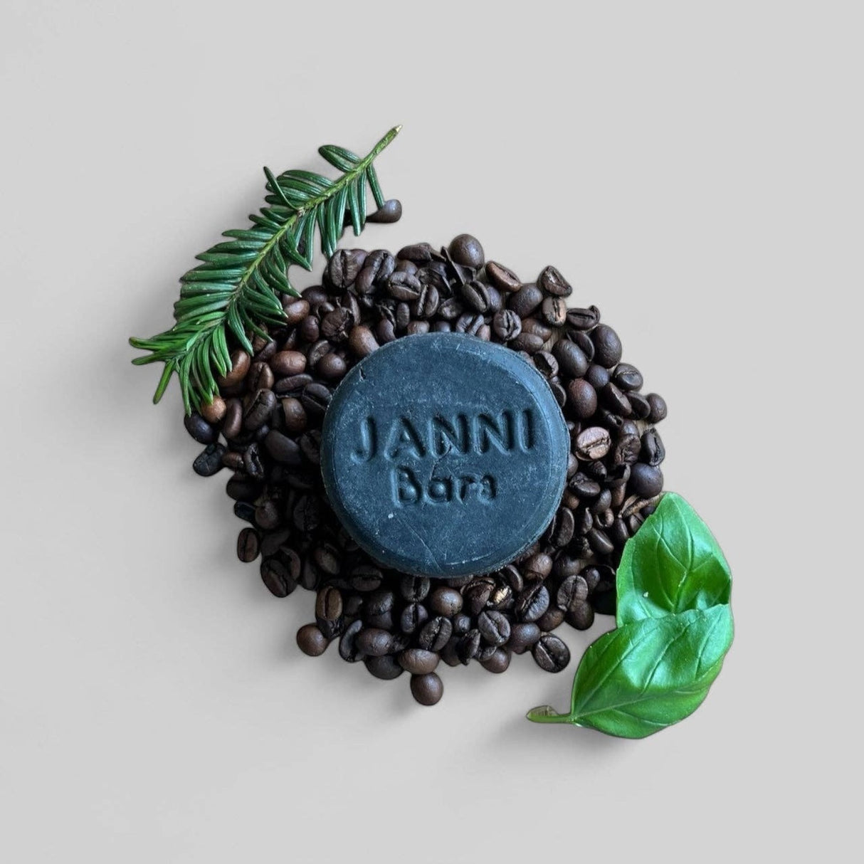 Connemara Country Janni Bars charcoal clarifying shampoo bar surrounded by coffee beans, pine needles, and basil leaves.