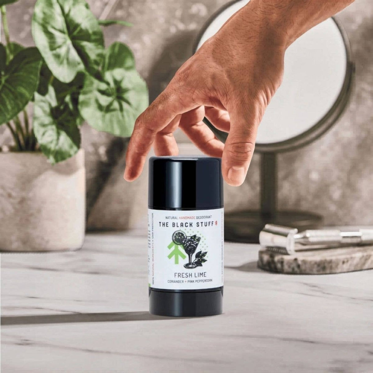 Connemara Country The Black Stuff natural deodorant in Fresh Lime scent held by a hand on a marble bathroom counter.