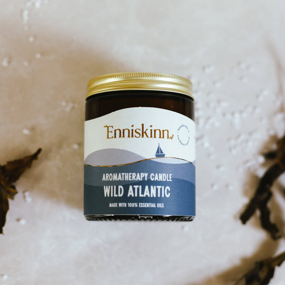 Connemara Country Enniskinn Wild Atlantic aromatherapy candle in a brown glass jar with a gold lid on a textured surface.